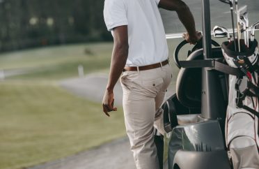 stylish african american man standing near golf cart on golf course